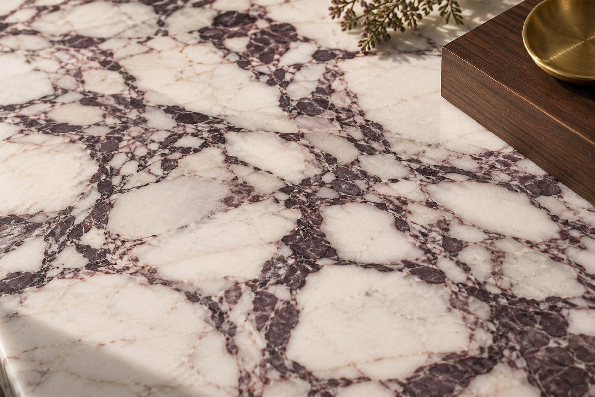 Close-up of Calacatta Viola marble with plum veins, next to walnut wood and a brass dish