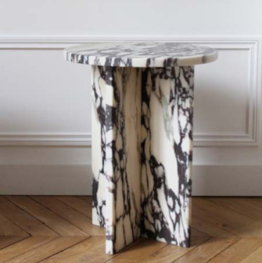 Round pale veined stone side table with intersecting slab supports beside a panelled wall
