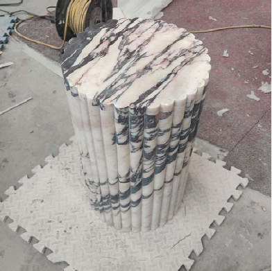 A round Calacatta Viola plinth with a scalloped outline and vertical fluting.