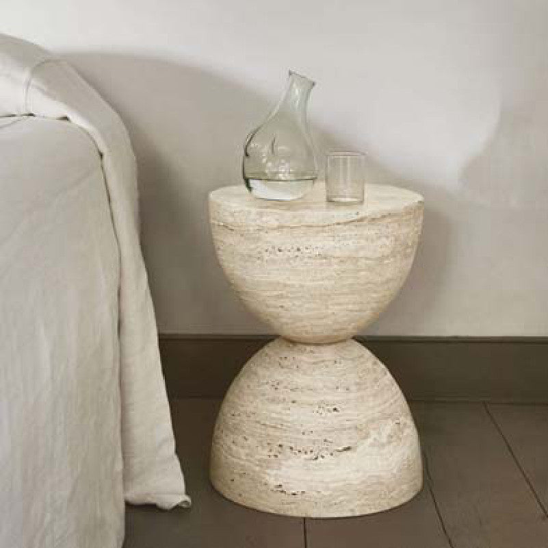 Beige stone side table with two curved halves forming an hourglass profile beside a sofa