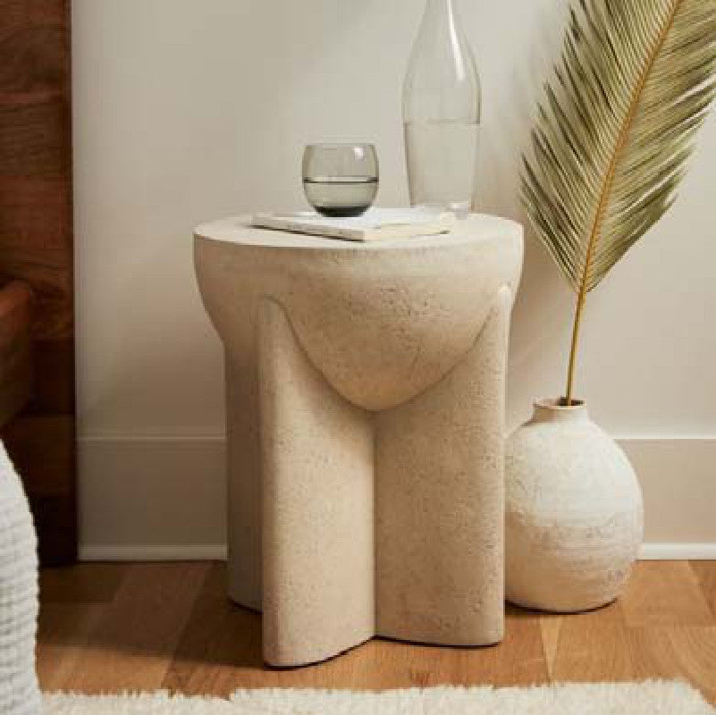 Travertine side table with sculpted intersecting supports beside a vase, front view