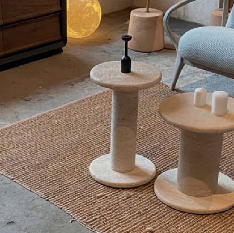 Two beige stone side tables with round tops, cylindrical stems and circular bases in a sitting room
