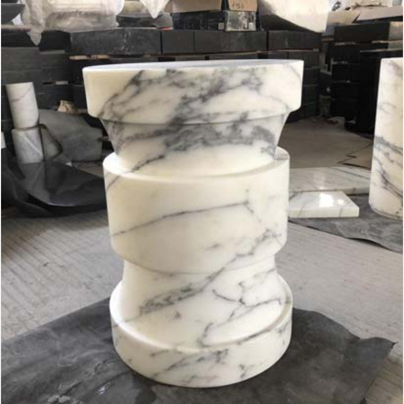 White and grey-veined stone side table with curved stacked sections photographed in a workshop