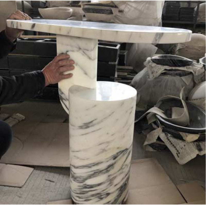 White and grey-veined stone side table with a round top and stepped pedestal in a workshop