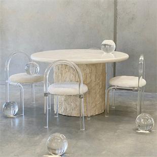 Round pale stone dining table with a textured cylindrical pedestal and transparent chairs