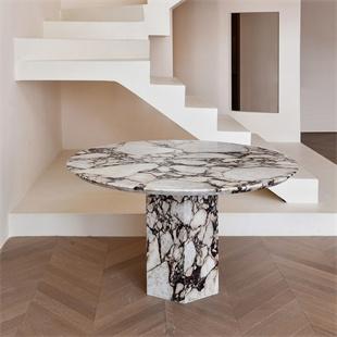 Round strongly veined stone dining table with a matching pedestal beside a staircase