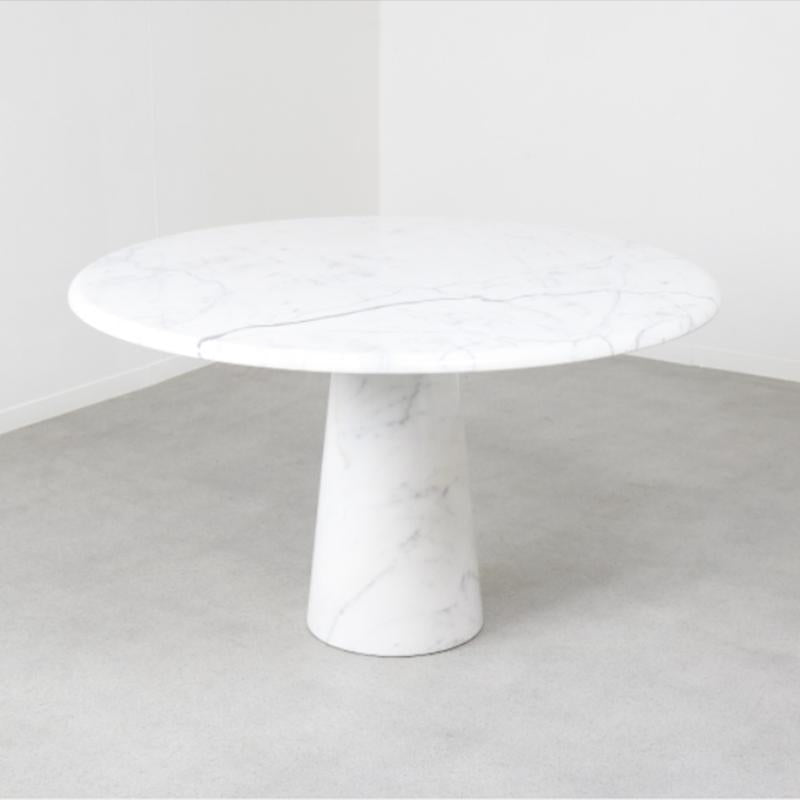 Round pale veined stone dining table with a tapered pedestal, three-quarter view