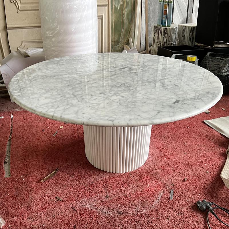 Round pale veined stone dining table with a fluted pedestal in a workshop
