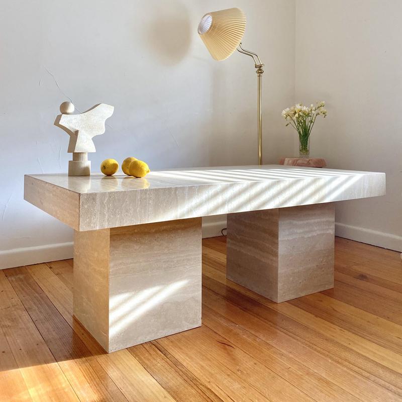 Rectangular pale stone table with a thick top and two block supports beside a floor lamp
