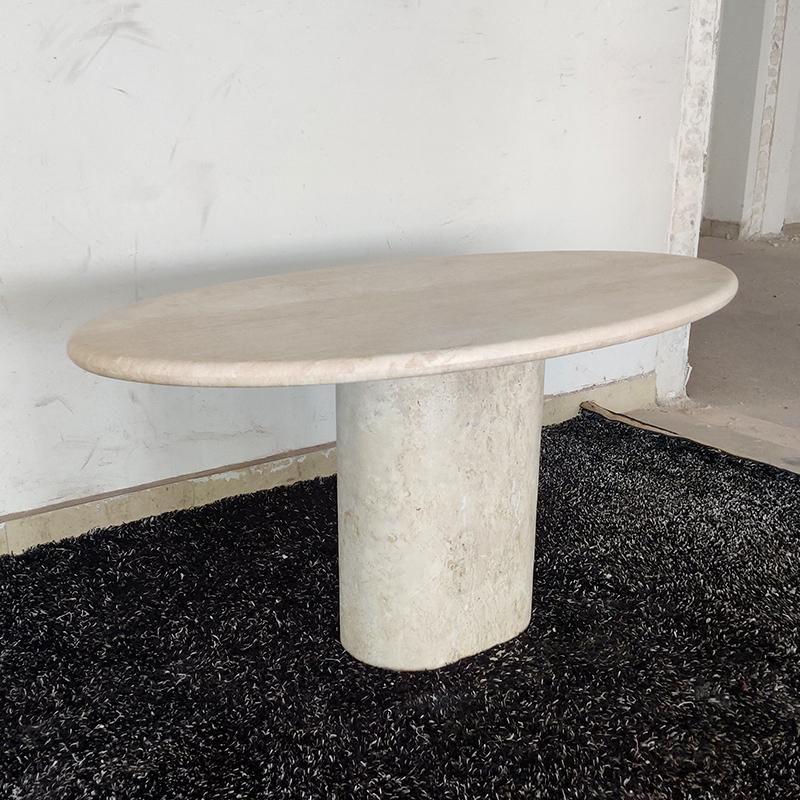 Oval pale stone dining table with a broad rounded pedestal, three-quarter view