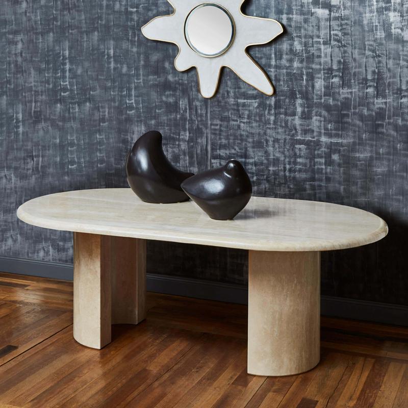 Oval pale stone table with two broad supports beneath a decorative mirror