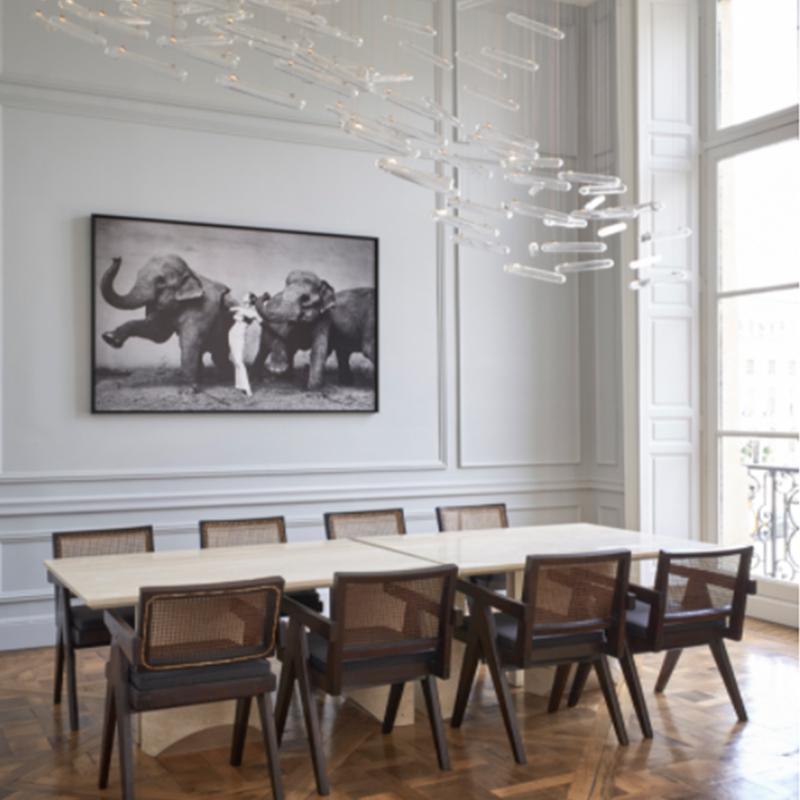 Rectangular pale stone dining table surrounded by wooden chairs beneath pendant lighting