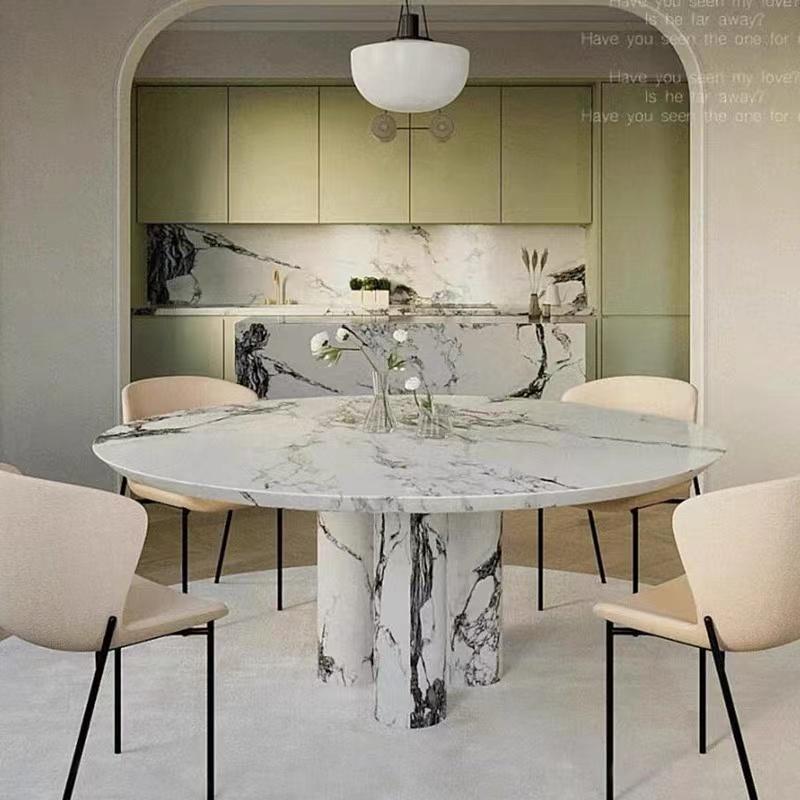 Round pale veined stone dining table with clustered legs and cream chairs in a dining room