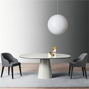 Round pale dining table with a tapered pedestal between two grey chairs beneath a pendant light