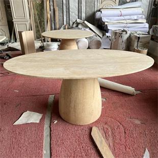 Oval beige stone dining table with a rounded pedestal in a workshop