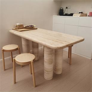 Rectangular pale stone table with rounded corners and clustered cylindrical legs beside stools