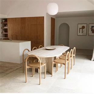 Oval pale stone dining table surrounded by wooden chairs in a dining room