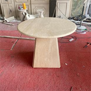 Round pale stone dining table with a tapered slab pedestal in a workshop