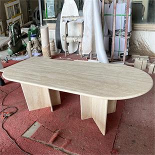 Oval stone dining table with pale veining and two slab supports in a workshop