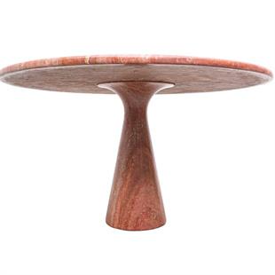 Round reddish stone dining table with a narrow sculptural pedestal, low-angle view