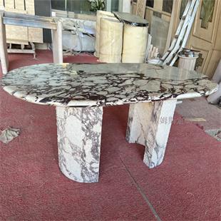 Oval veined stone dining table with two broad supports in a workshop