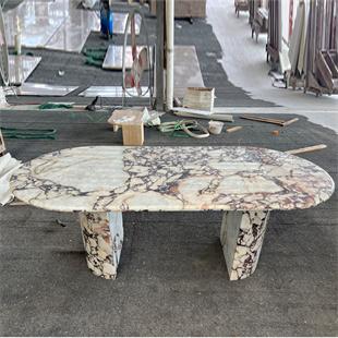 Oval stone dining table with dark veining and two slab supports in a workshop