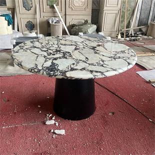 Round veined stone dining table with a dark cylindrical pedestal in a workshop