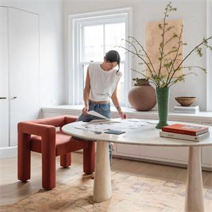 Pale veined stone table with cylindrical legs beside red chairs and a person, cropped room view