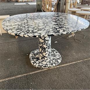 Round stone dining table with a black and white patterned pedestal in a workshop
