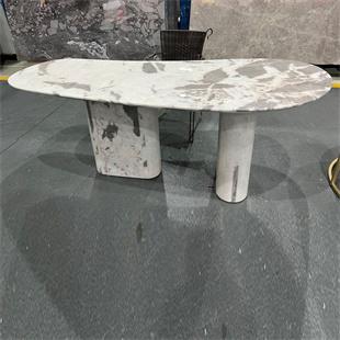 Oval pale veined stone dining table with broad supports in a showroom