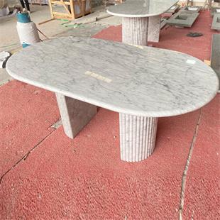 Oval pale veined stone dining table with fluted supports in a workshop