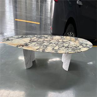 Oval stone dining table with a strongly patterned top and two pale supports in a workshop