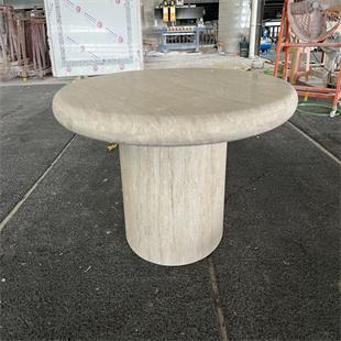 Round pale stone dining table with a thick rounded edge and cylindrical pedestal in a workshop