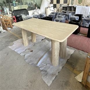 Rectangular beige stone dining table with rounded corners and fluted legs in a workshop
