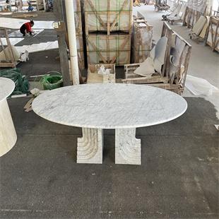 Oval pale stone dining table with two sculpted slab supports in a workshop