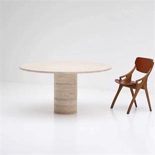 Round pale stone dining table with a cylindrical pedestal beside a wooden chair