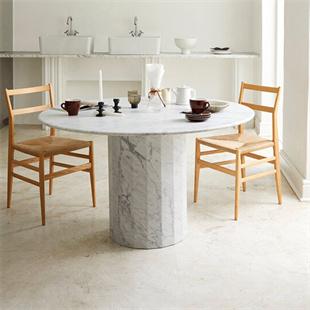 Round pale veined stone dining table with wooden chairs in a bright dining room