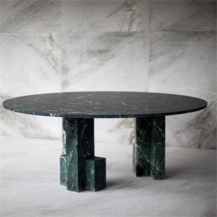 Round dark stone dining table with two geometric green-toned supports, three-quarter view