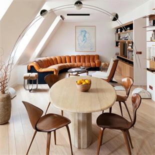Oval pale stone dining table with a fluted pedestal and wooden chairs beneath a sloping ceiling