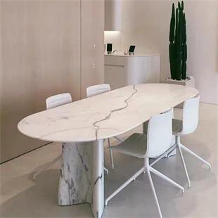 Oval pale veined stone dining table with white chairs beside a tall cactus