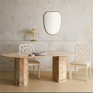 Oval pale stone dining table with two broad supports and cream chairs in a dining room