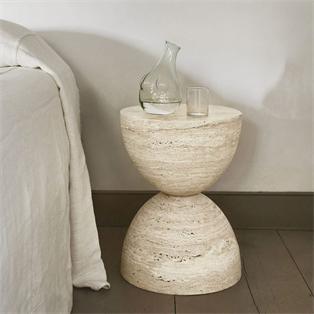 Pale stone side table with an hourglass silhouette beside an upholstered sofa