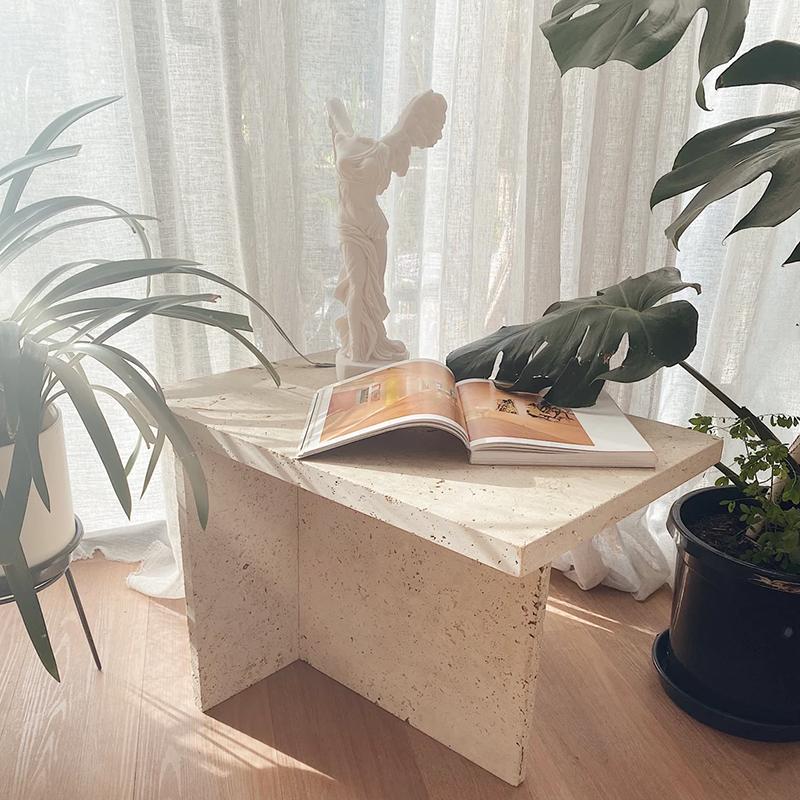 Pale stone table with a triangular top and intersecting slab supports beside plants