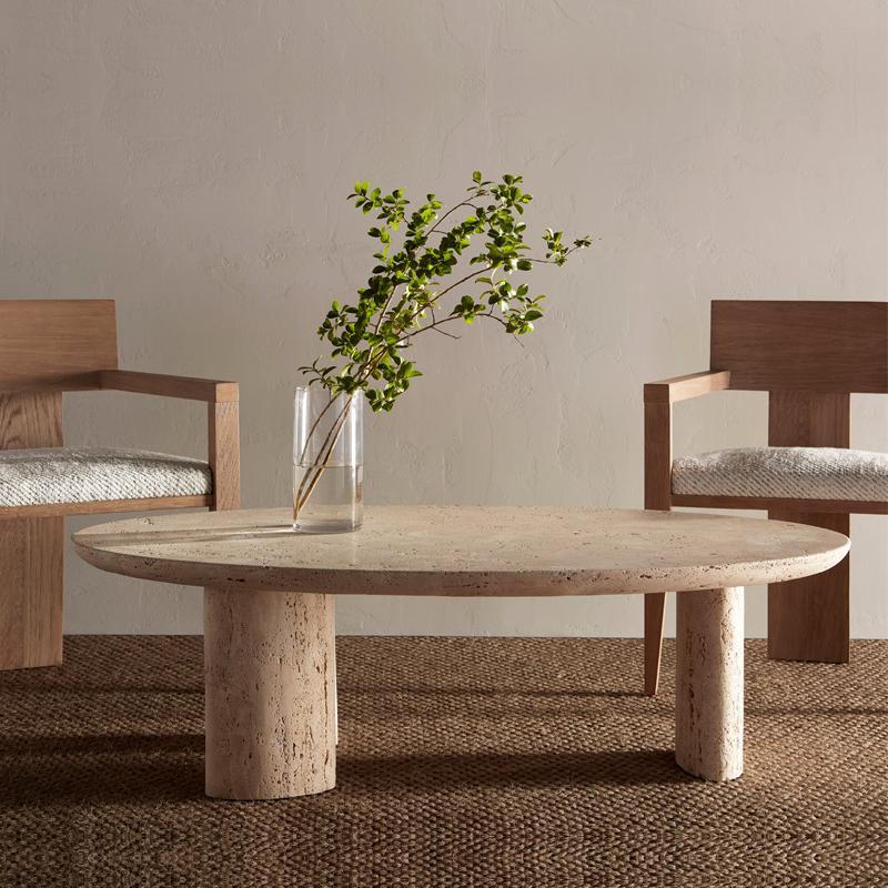 Oval pale stone coffee table with cylindrical legs between two armchairs
