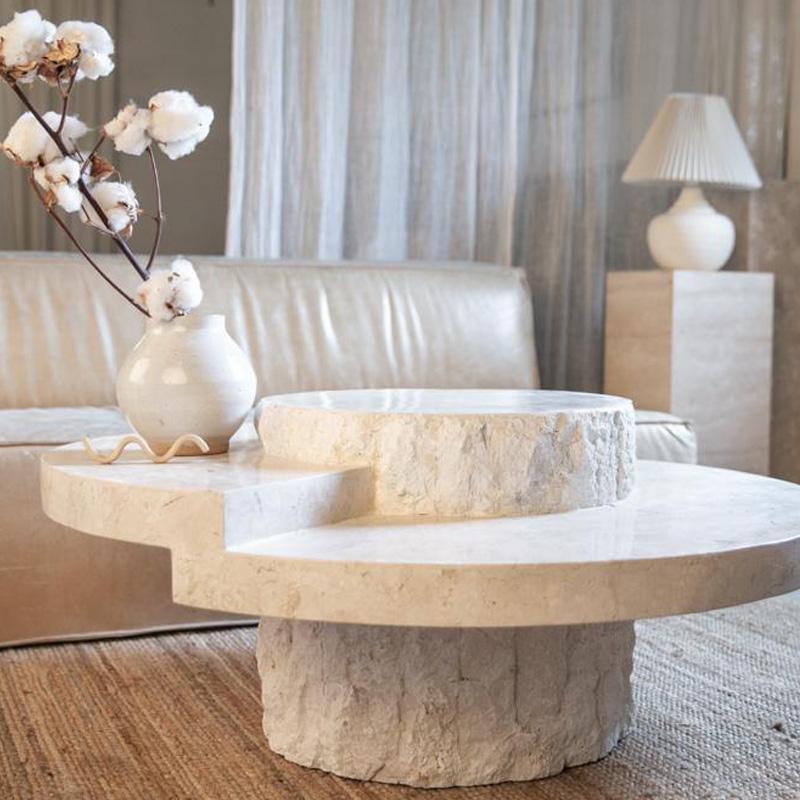 Pale stone coffee table with a stepped curved top and rough cylindrical base beside a sofa