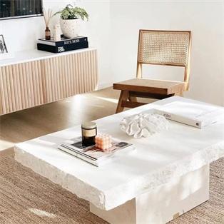 Rectangular pale stone coffee table with a rough-textured edge beside a wooden chair