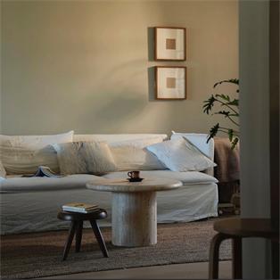 Round pale stone coffee table with a cylindrical pedestal in front of a sofa