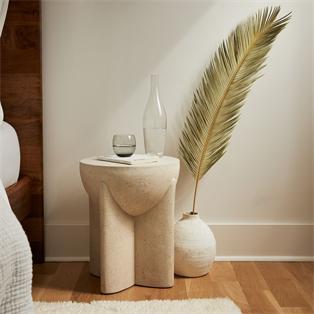 Pale stone side table with sculpted intersecting supports beside a vase, front view
