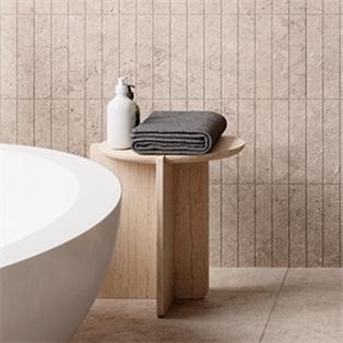 Round pale stone side table with intersecting slab supports beside a bath