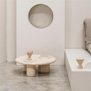 Round pale stone coffee table with cylindrical supports beside a sofa and a circular wall recess
